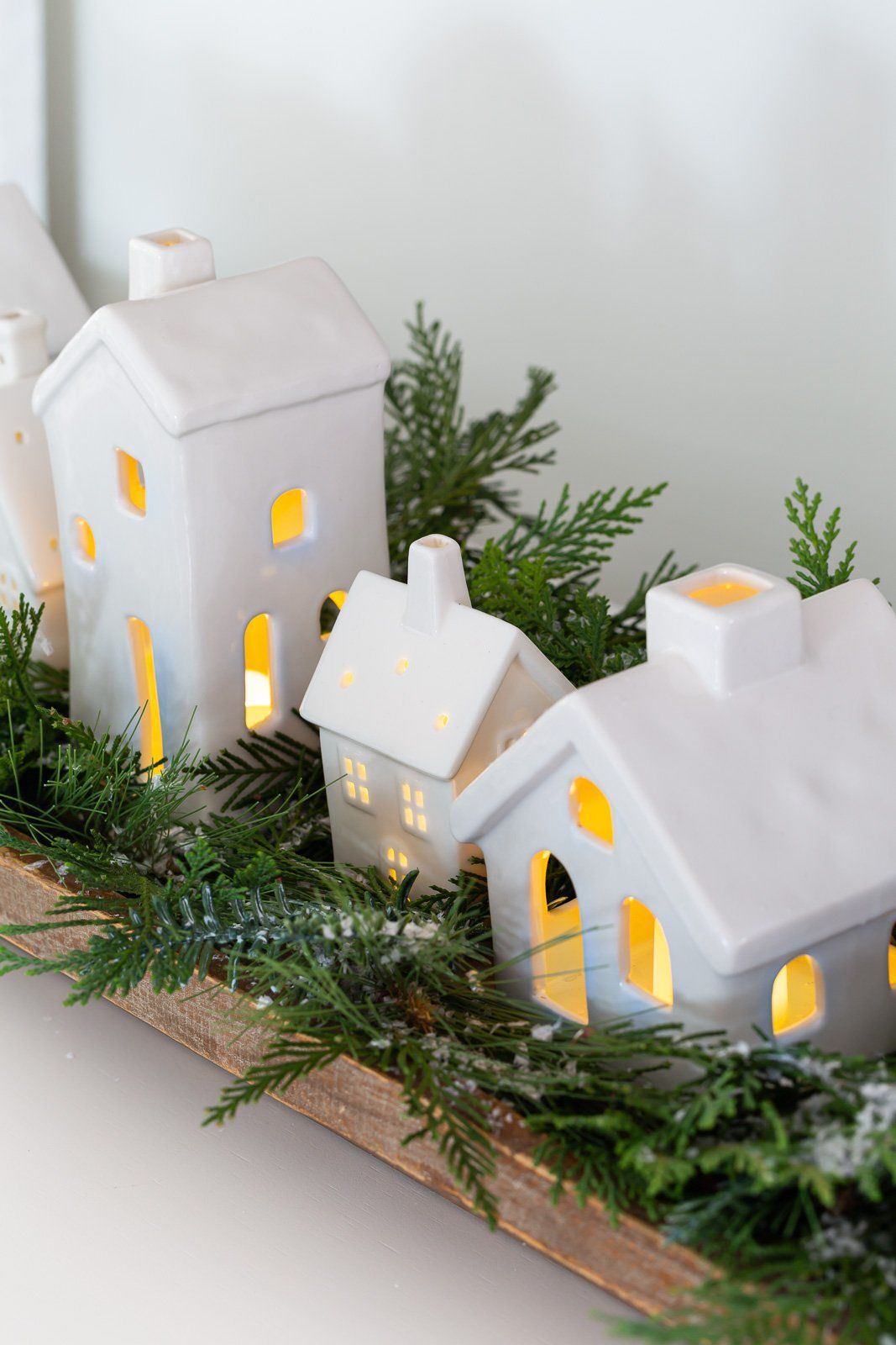 Long dough bowl with a row of glowing white ceramic houses nestled in evergreen branches