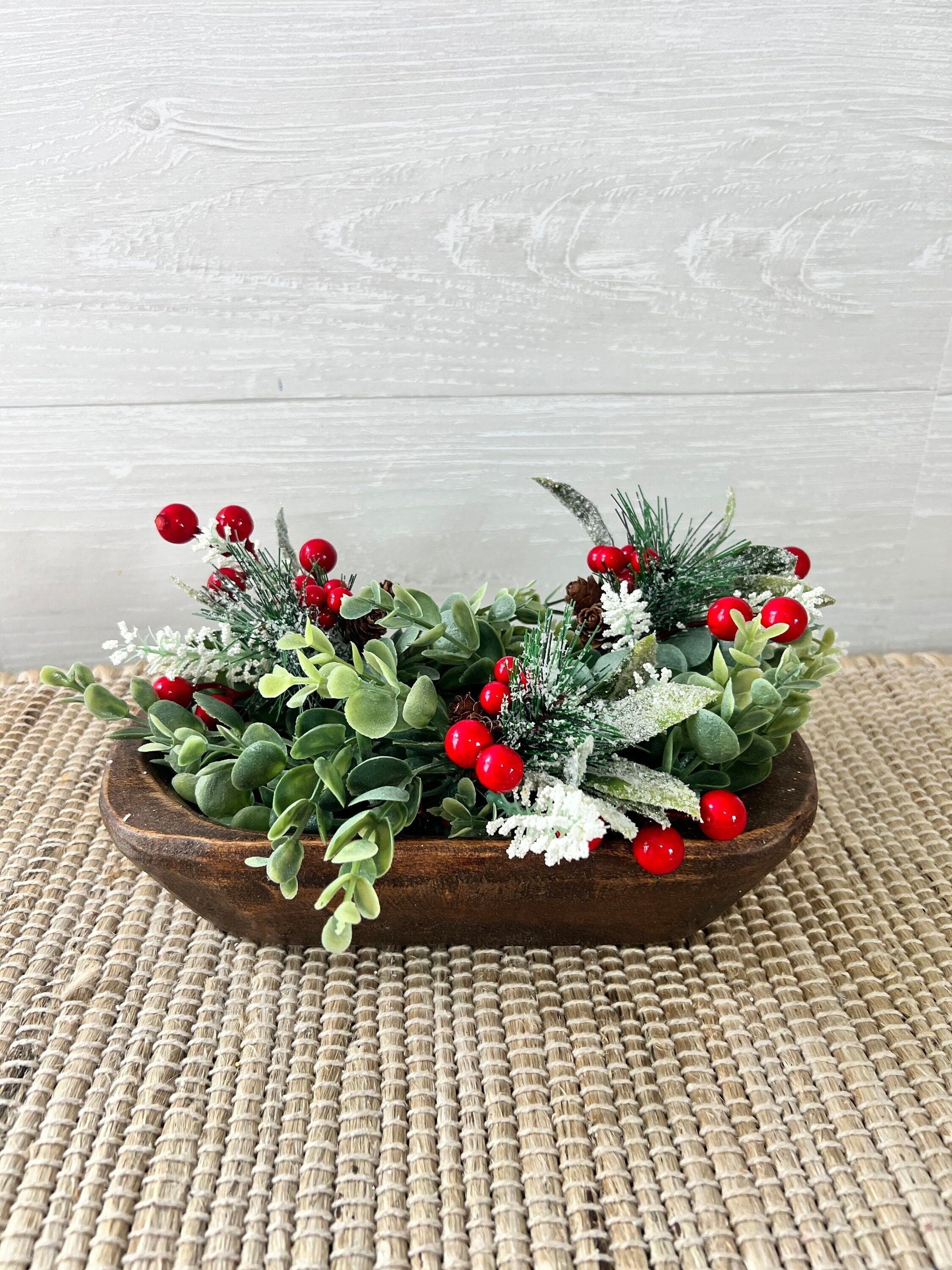 Dark wood dough bowl filled with faux boxwood, frosted greenery and clusters of bright red winter berries