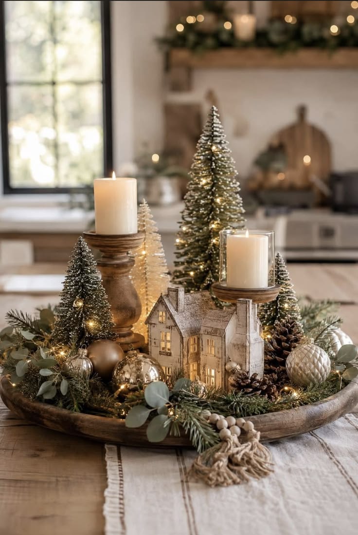 Round wooden tray with candles in turned holders, a small village house, bottle brush trees, ornaments and eucalyptus