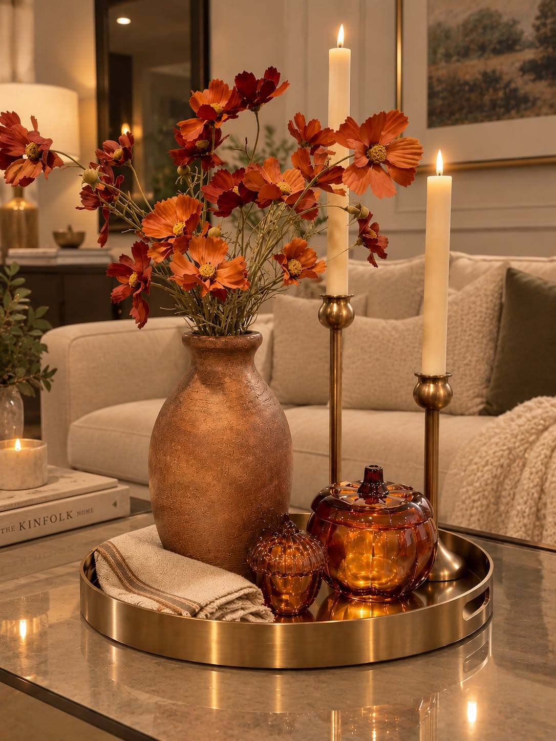 Tray with amber glass candles and a copper vase of orange flowers