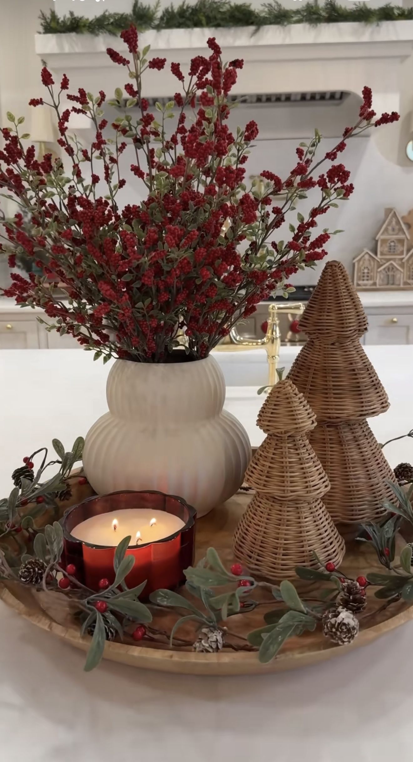 Round wood tray with two wicker trees, a cream vase of red berry branches and a candle in a red glass holder