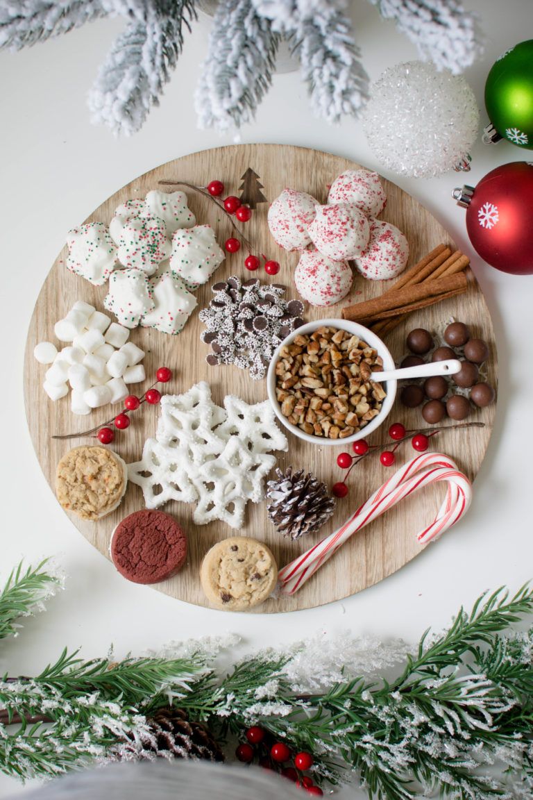 Round wood board of cookies, snowflake pretzels, marshmallows, nuts and candy with a candy cane